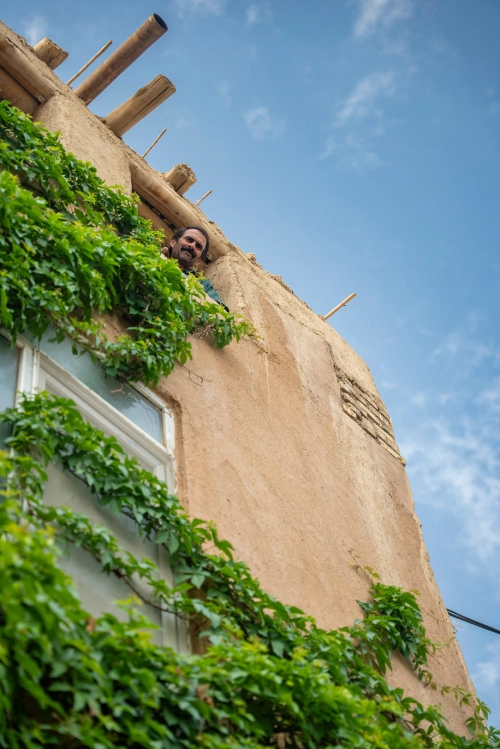 Man looking out of a window of a green village house